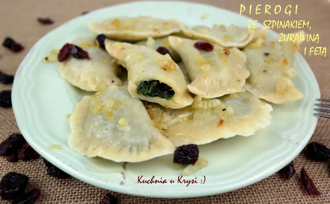 Pyszne pierogi ze szpinakiem i serem feta, okraszone cebulką i żurawiną, na talerzu.