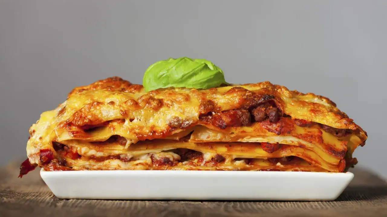 Una porción generosa de lasagna italiana, con capas de pasta, carne y queso derretido, coronada con una hoja de albahaca fresca.