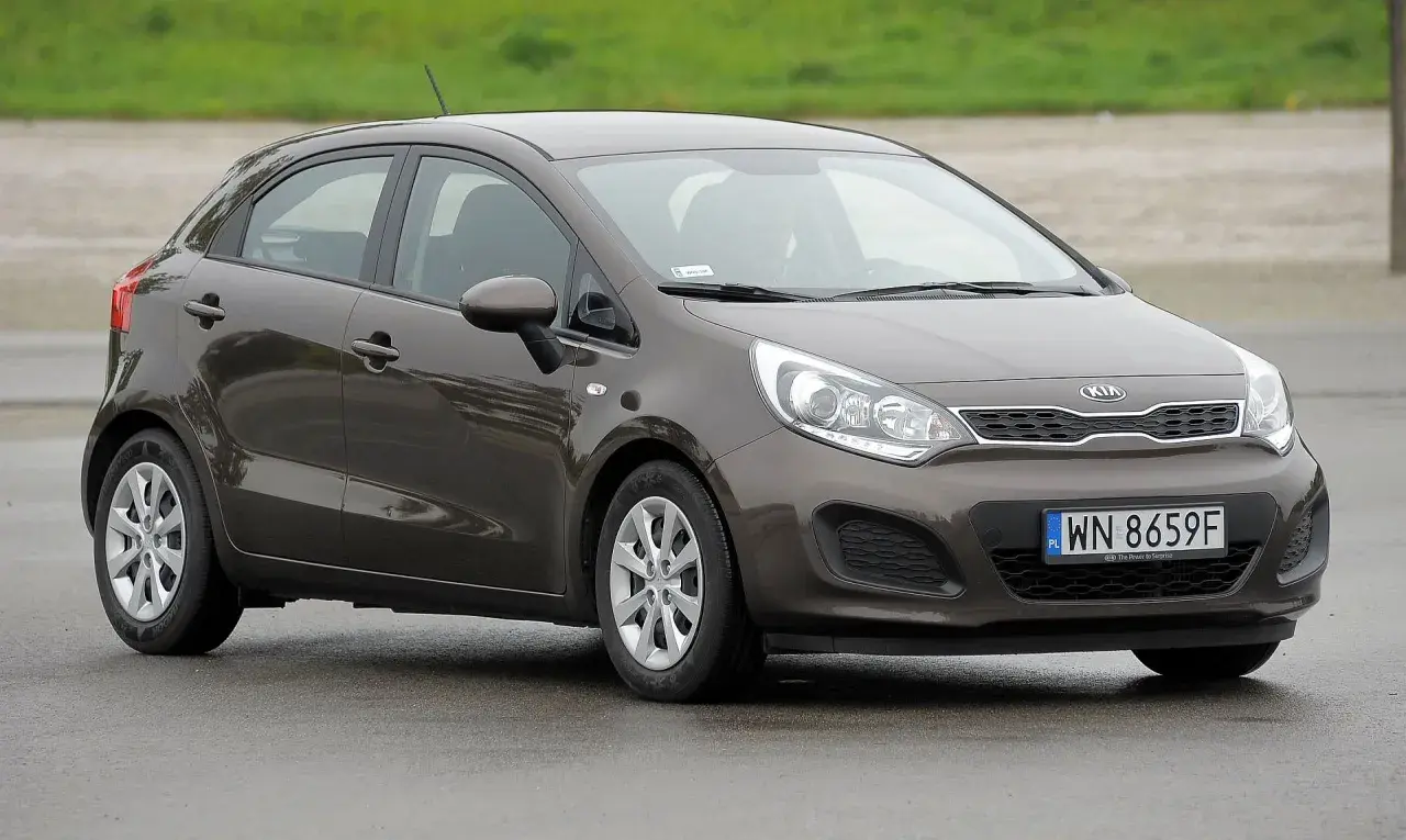 Brązowe kia rio 3 na mokrej nawierzchni, z widocznym numerem rejestracyjnym WN 8659F.