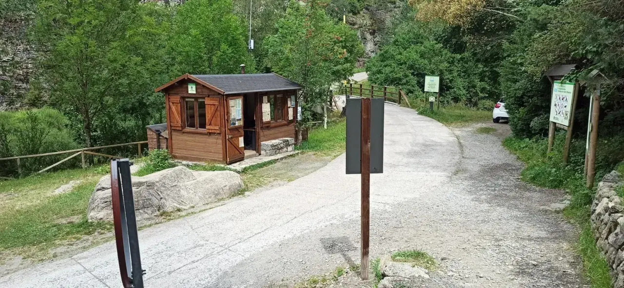 Caseta de información y señalización para senderismo en Aigüestortes. Un camino de grava y asfalto se adentra en un bosque frondoso.