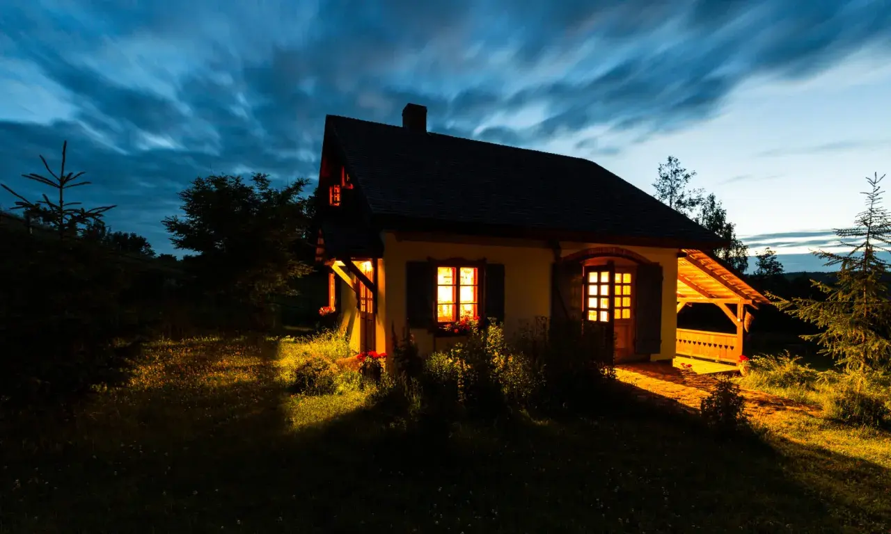 Przytulny domek na cisowym wzgórzu, oświetlony ciepłym światłem z okien, na tle rozmytego, granatowego nieba.