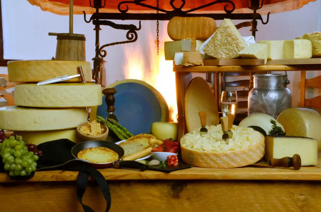 Un'abbondante tavola di formaggi, con una grande forma scavata che ricorda una fonduta di caprino, accompagnata da uva, fragole e pane tostato.