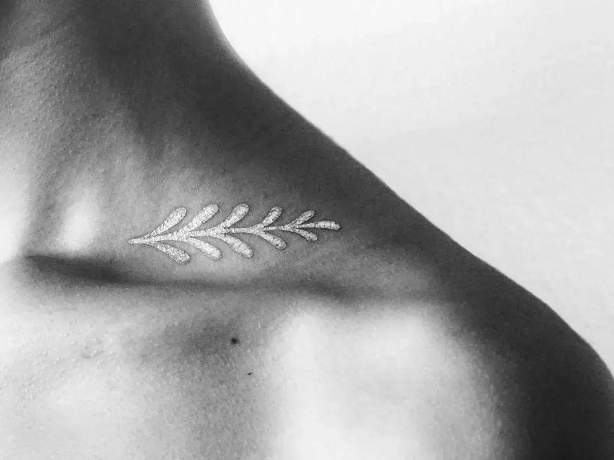 Delicado diseño de rama con **tatuajes blancos en piel negra**, resaltando la delicadeza y el contraste en el hombro.
