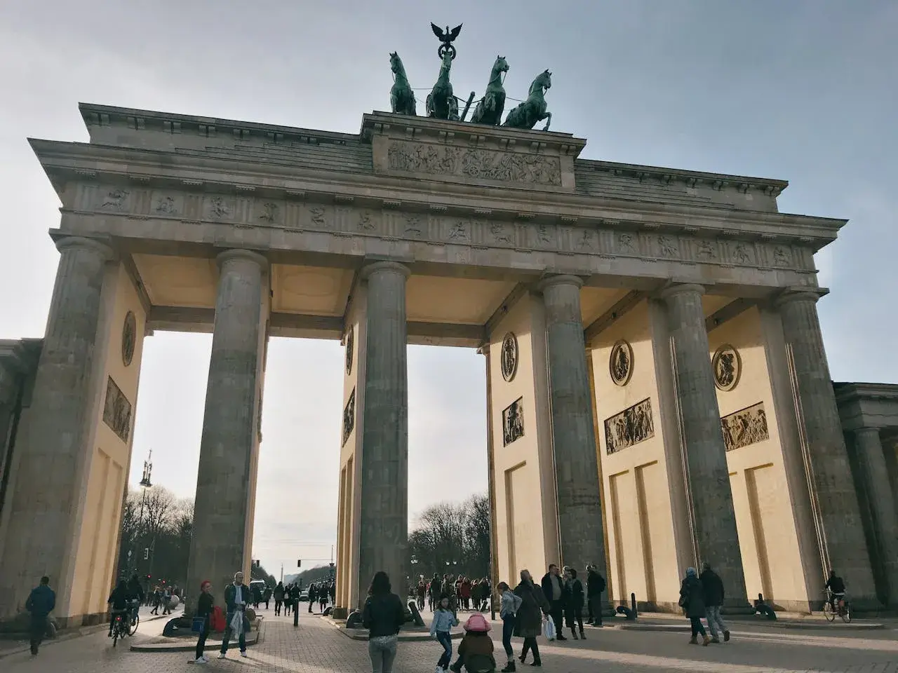 Das Brandenburger Tor, ein Meisterwerk der Klassizismus Architektur, mit seiner Quadriga auf dem Dach. Menschen spazieren davor.