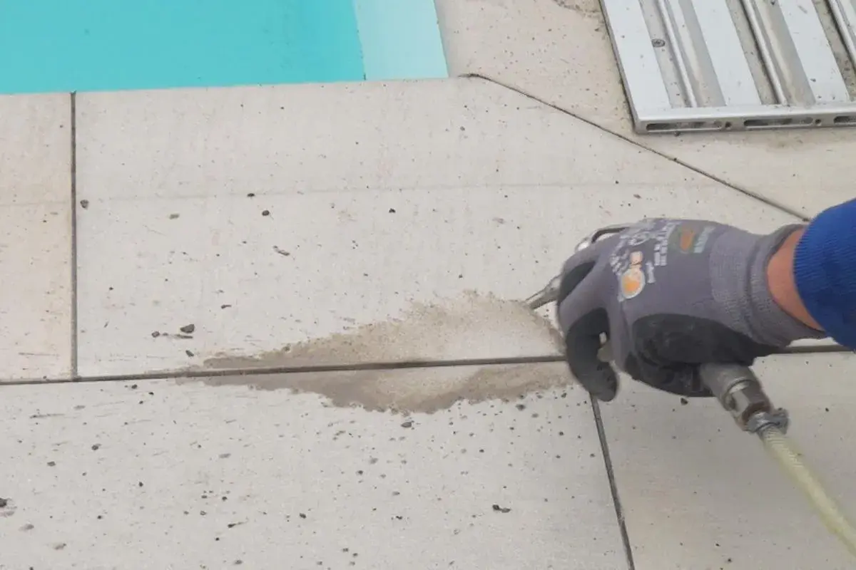 Arbeiter erneuert mit Sprühpistole die Silikonfugen auf gefliestem Boden neben einem Pool.