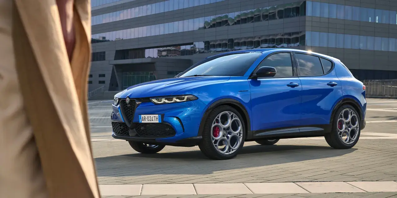 Niebieskie Alfa Romeo Tonale błyszczy na tle nowoczesnego budynku. Sprawdź aktualną alfa romeo tonale cena i odkryj jego możliwości.