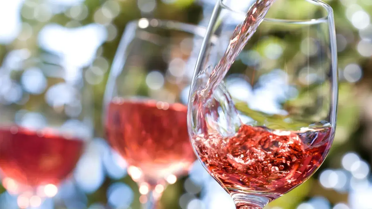 Vin rosé versé dans un verre, avec d'autres verres en arrière-plan flou.