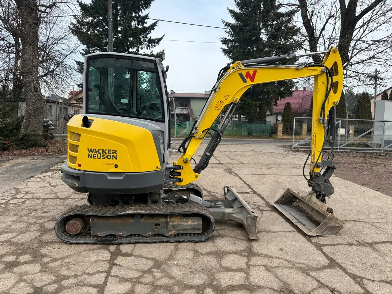 Żółta minikoparka Wacker Neuson z kabiną stoi na placu.