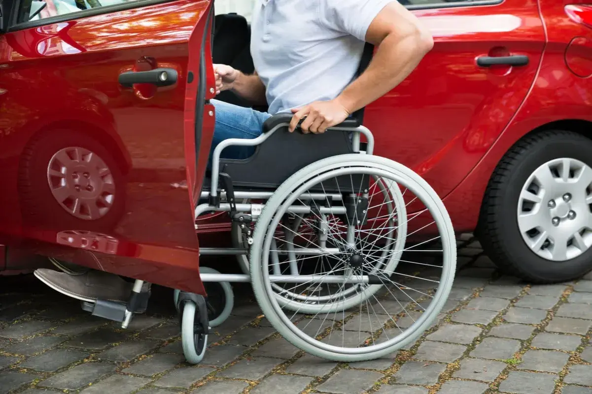 Persona in sedia a rotelle si avvicina a un'auto rossa, modello 104, per salire.