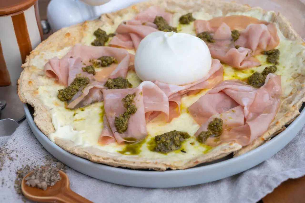 Pizza mit Burrata, Mortadella und Pesto auf einem Teller.