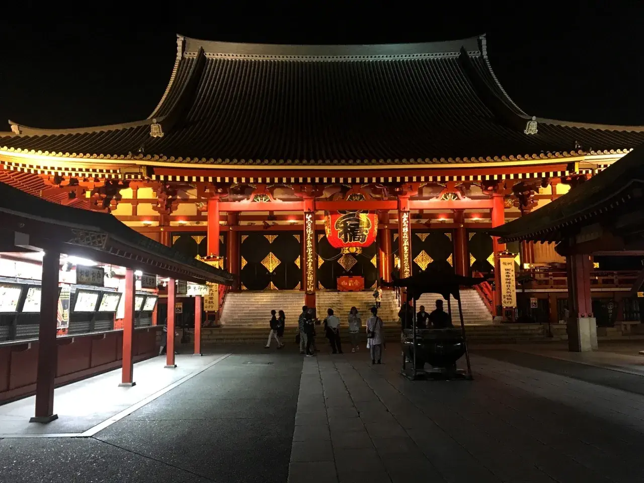 Nocny widok na świątynię Senso-ji z czerwoną latarnią i ludźmi spacerującymi po dziedzińcu.