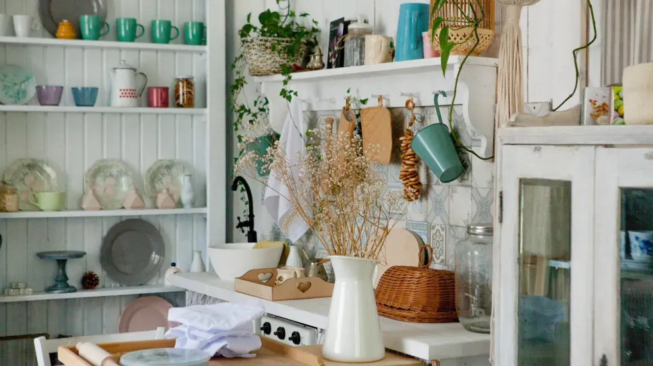 A cozy granny chic kitchen with shelves full of colorful mugs, plates, and jars. A bouquet of dried flowers adds a rustic touch.