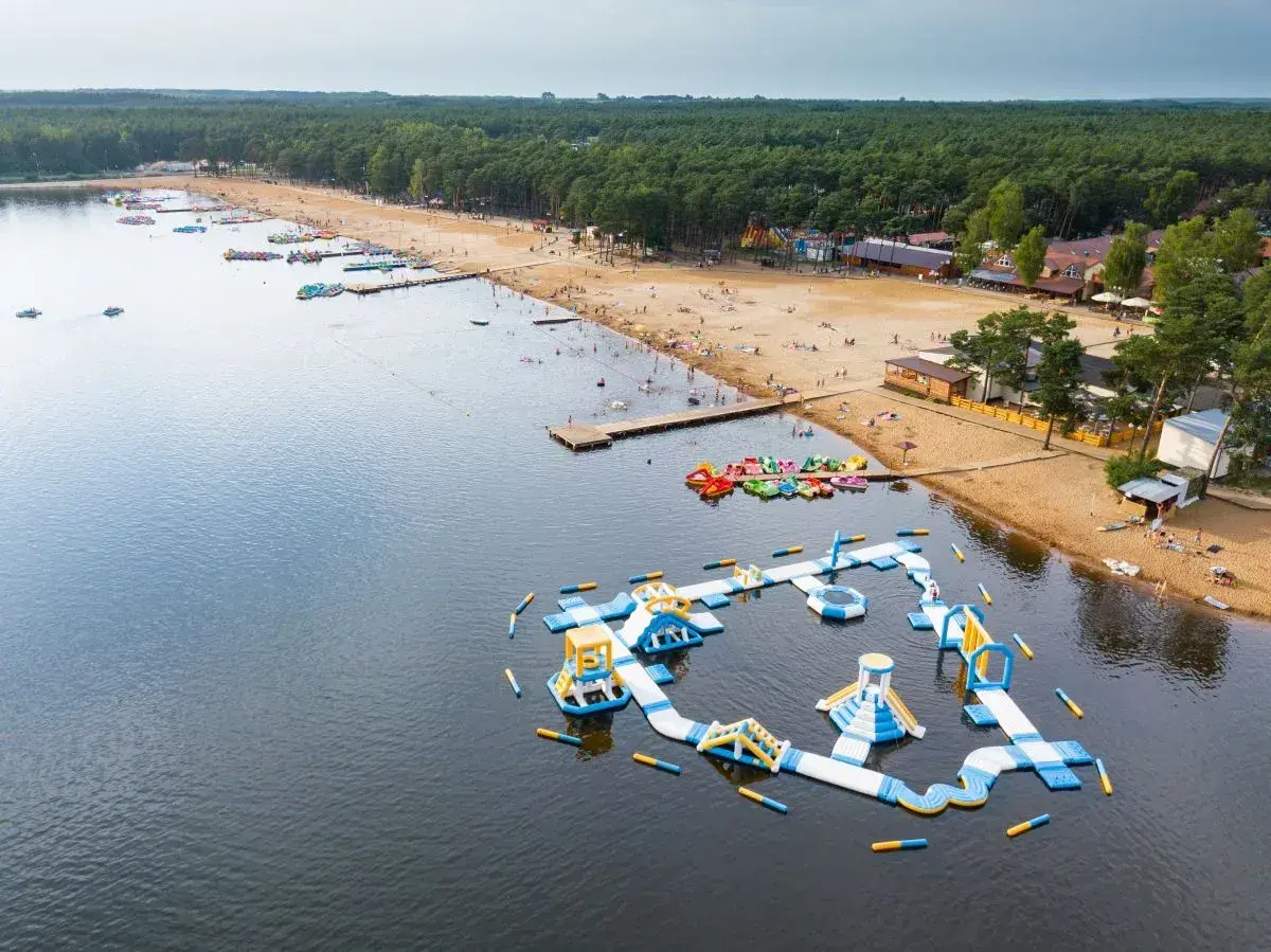 Sielpia atrakcje: dmuchany plac zabaw na wodzie, plaża z ludźmi, wypożyczalnia sprzętu wodnego i las.
