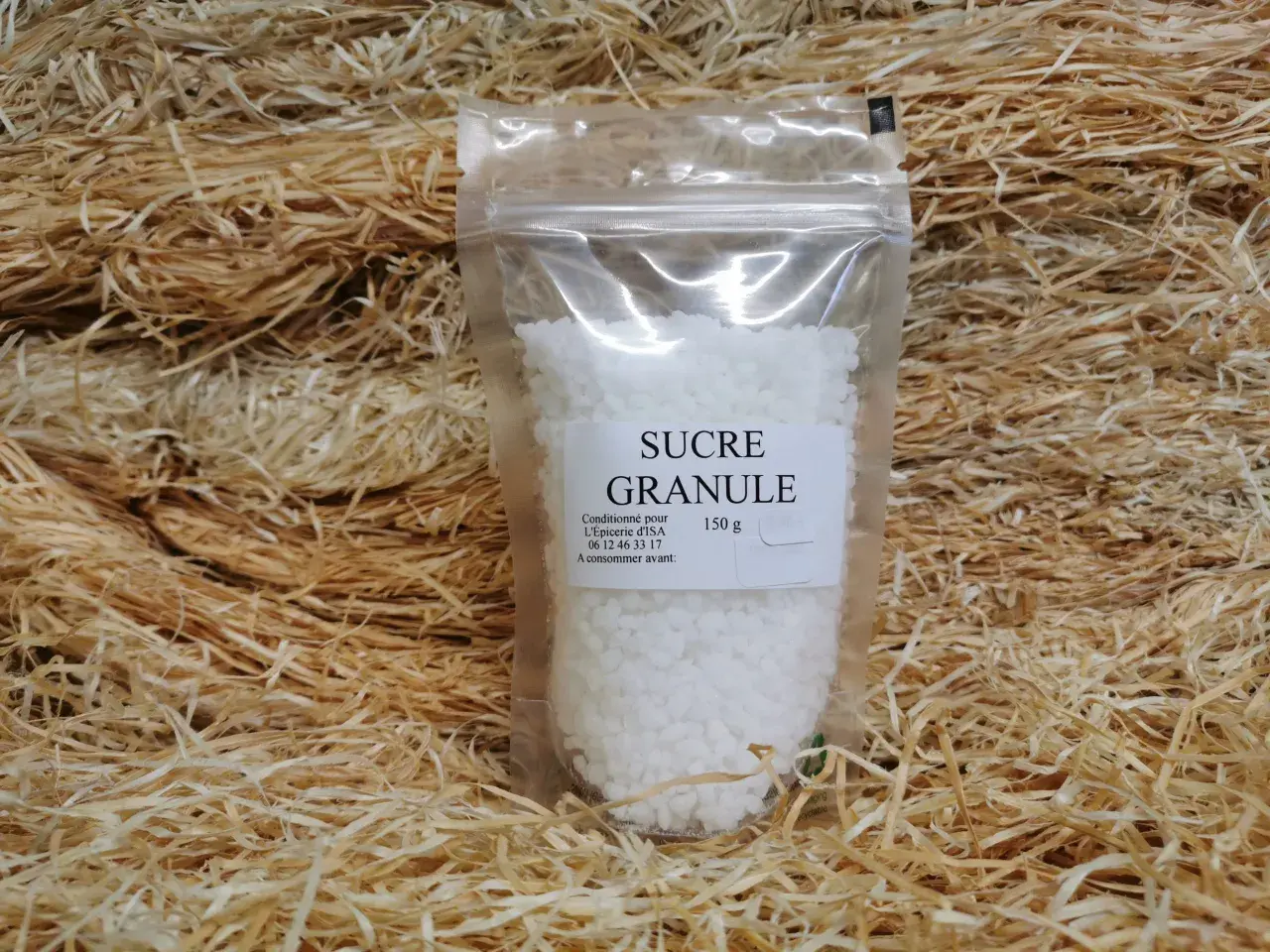 Un sachet de sucre granulé, 150g, est présenté sur un lit de copeaux de bois. Ce sucre granulé, c'est quoi ? C'est du sucre cristallisé.