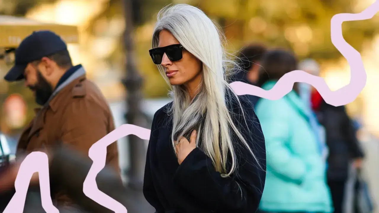 Mujer con pelo blanco largo y liso, gafas de sol oscuras y abrigo negro. La moda pelo blanco mujer es tendencia.