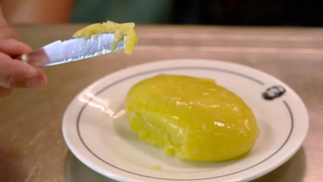 Un cuchillo recoge una porción de cremoso alioli casero, listo para untar sobre un plato blanco.
