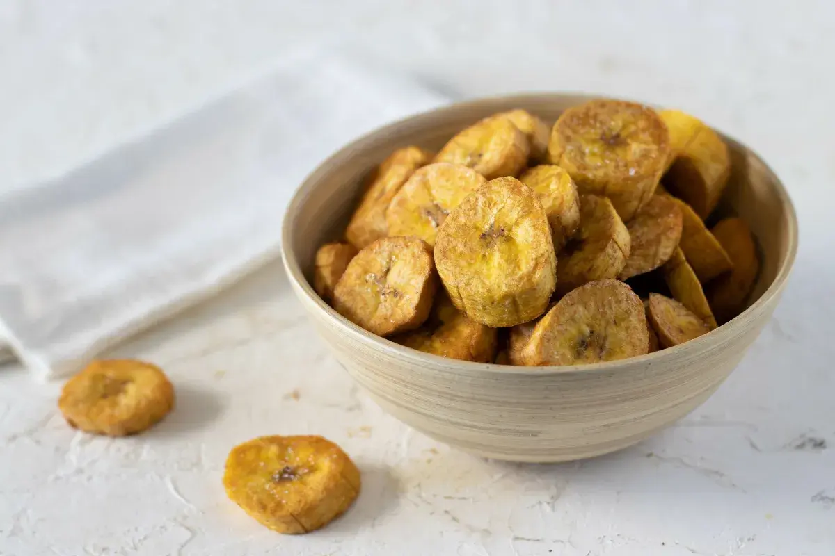 Un tazón de crujientes rodajas de plátano frito, espolvoreadas con sal, listas para disfrutar.