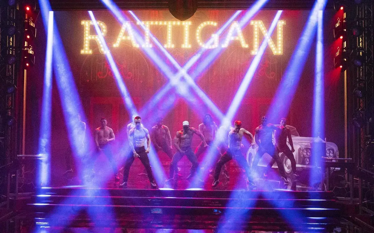 Mężczyźni tańczą na scenie w świetle niebieskich reflektorów, pod neonowym napisem "RATTIGAN". To scena z filmu Magic Mike 1.