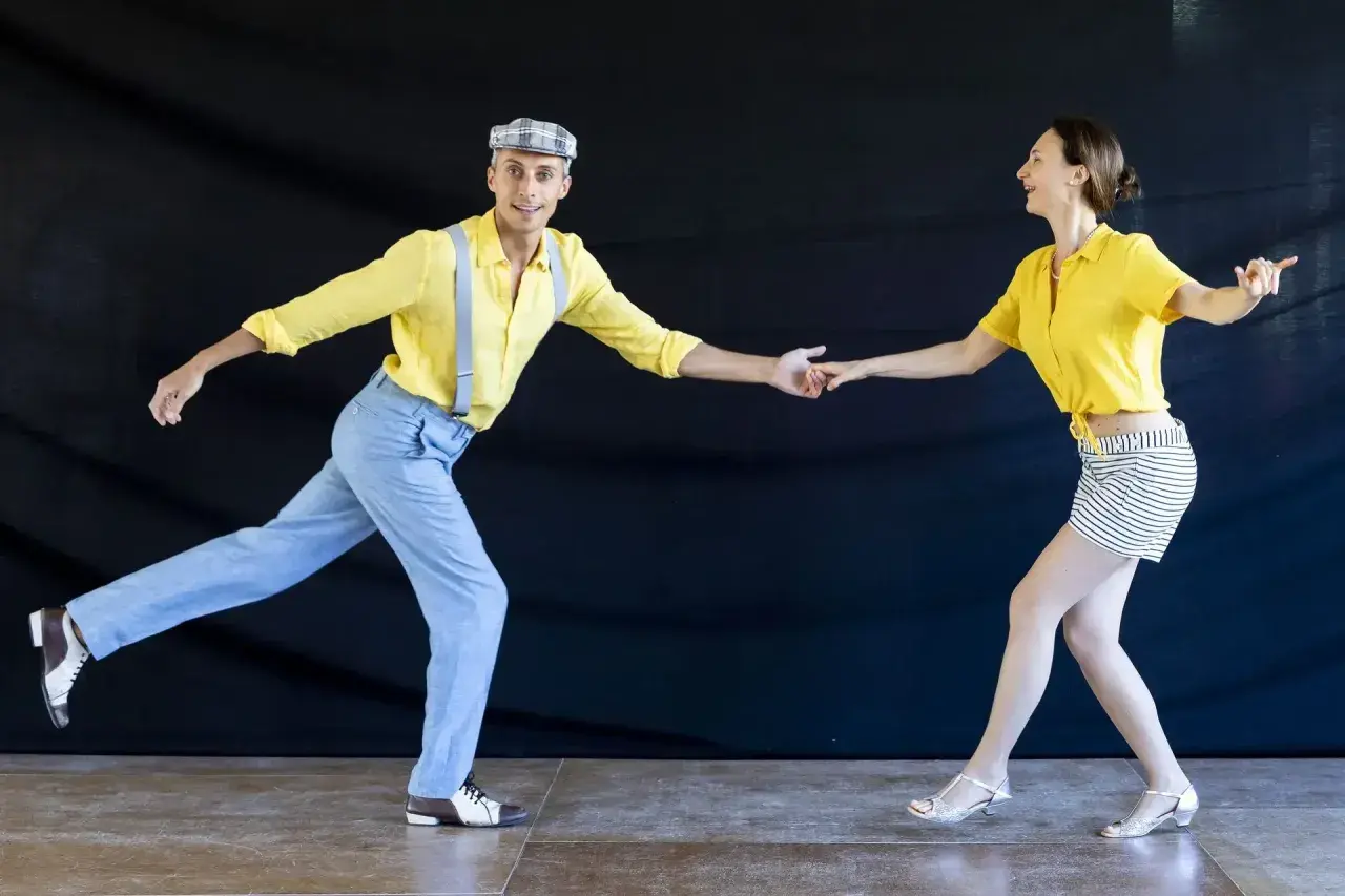 Coppia in abiti vintage che esegue un energico lindy hop ballo, con lui in giallo e bretelle, lei in giallo e gonna a righe.