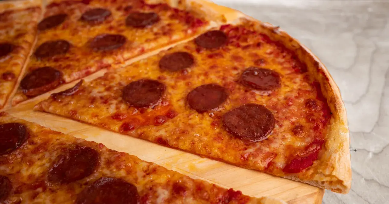 Kawałki pizzy pepperoni z roztopionym serem na desce.