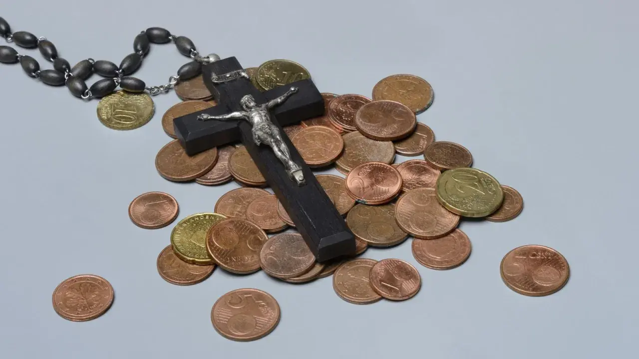 Holzkreuz mit Korpus, Rosenkranz und Münzen. Ein Symbol für das Kirchgeld in Bayern.