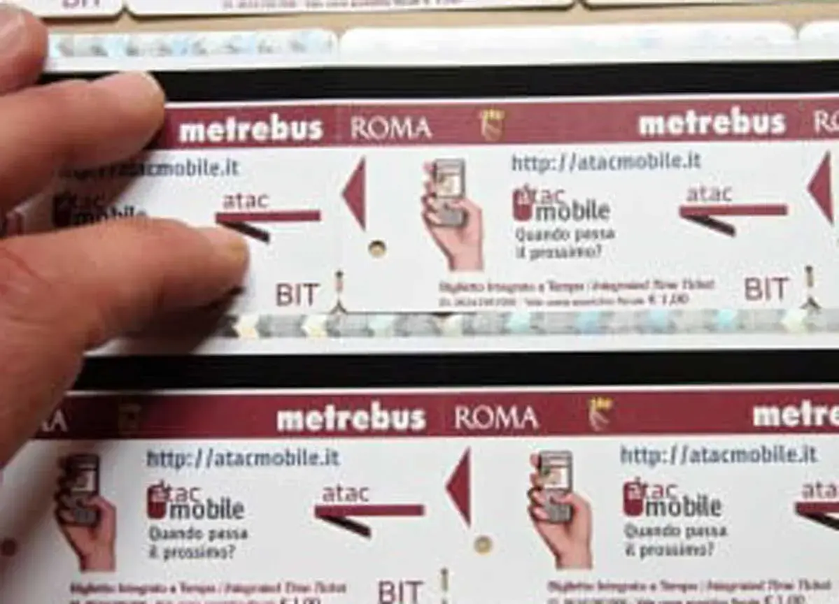 Dita sfiorano un biglietto metro Roma da 2 euro, con logo Atac e indicazioni per l'acquisto online.