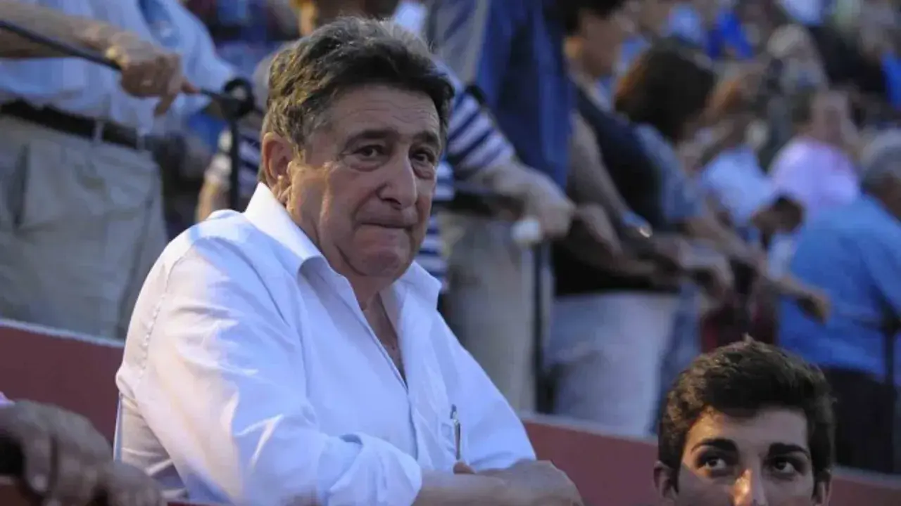 Hombre mayor con camisa blanca, posible dueño de ganadería Domingo Hernández, observa atentamente en una plaza de toros.