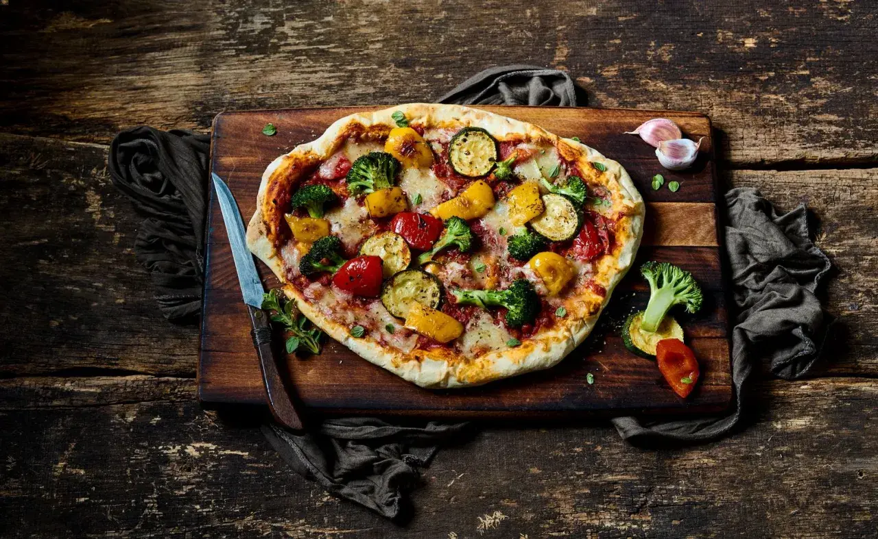 Eine köstliche vegane Pizza mit buntem Gemüse-Belag: Brokkoli, Zucchini, Paprika und Tomaten.