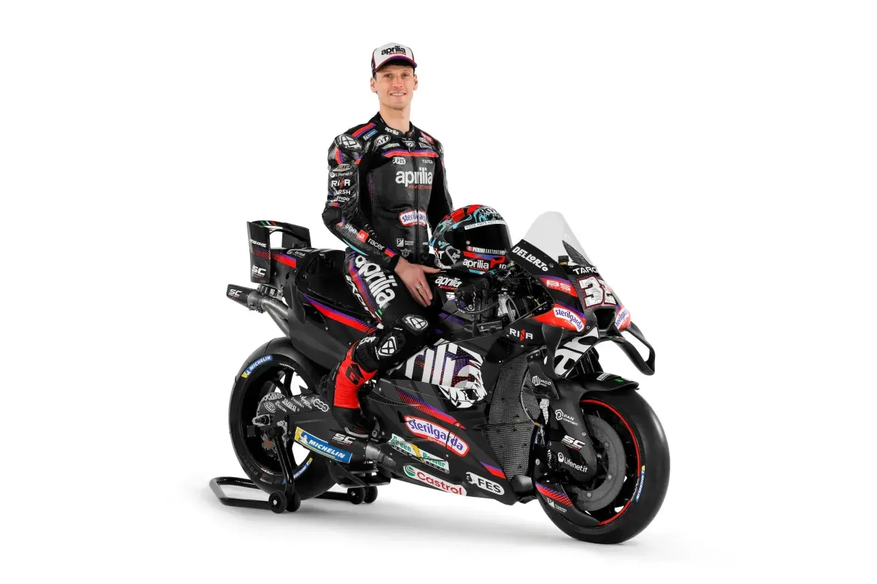 Piloto de Aprilia MotoGP posa junto a su moto de carreras negra y roja, listo para la acción.