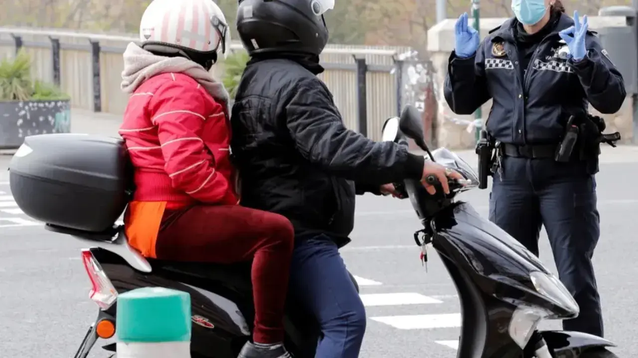 Agente de policía detiene a pareja en moto. Podrían recibir una multa por ir sin casco.