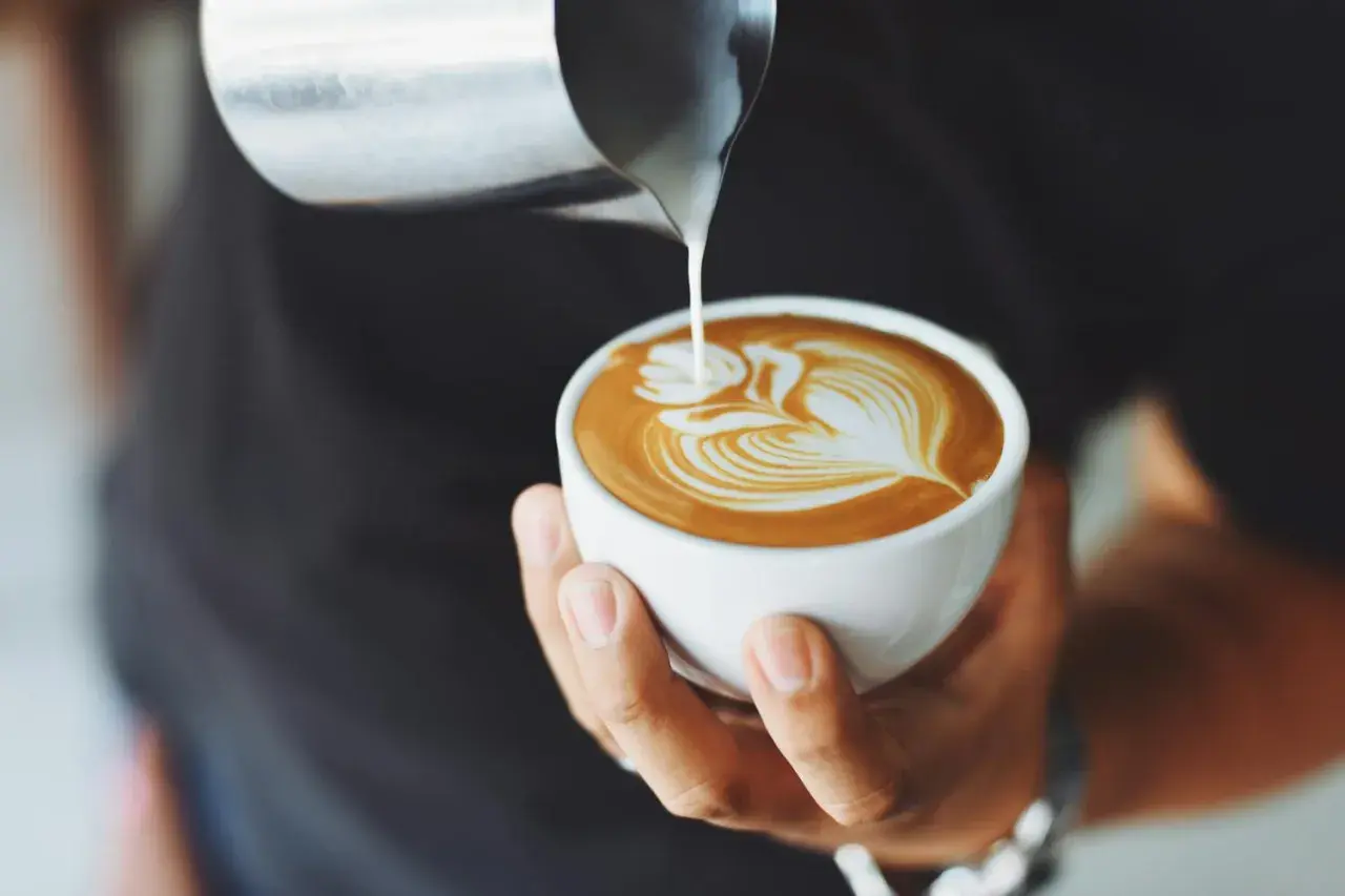 Mistrz tworzy latte art, idealne latte proporcje. Mleko wlewa się do kawy, tworząc wzór.
