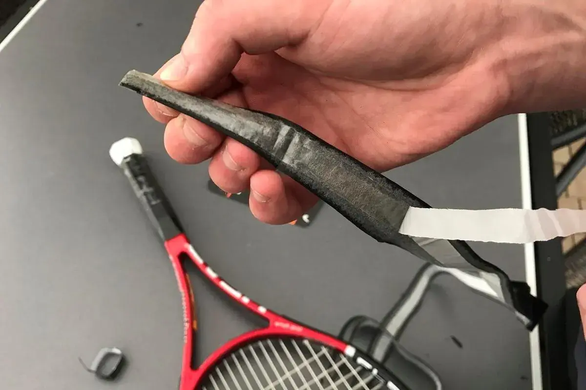 Dłoń trzyma starą, zużytą owijkę squash, która jest odklejana od rakiety.