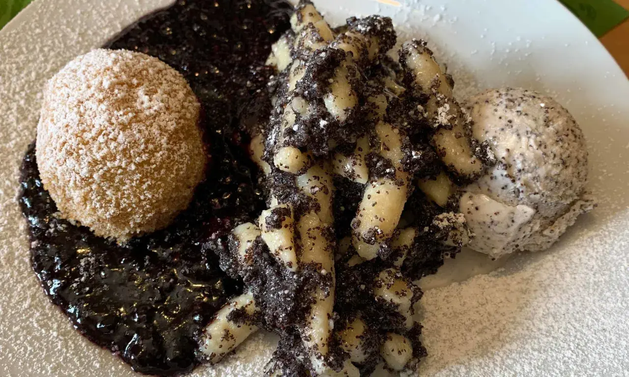Gedrehte Nudeln mit Mohn, eine Kugel und Beerensoße, bestäubt mit Puderzucker.