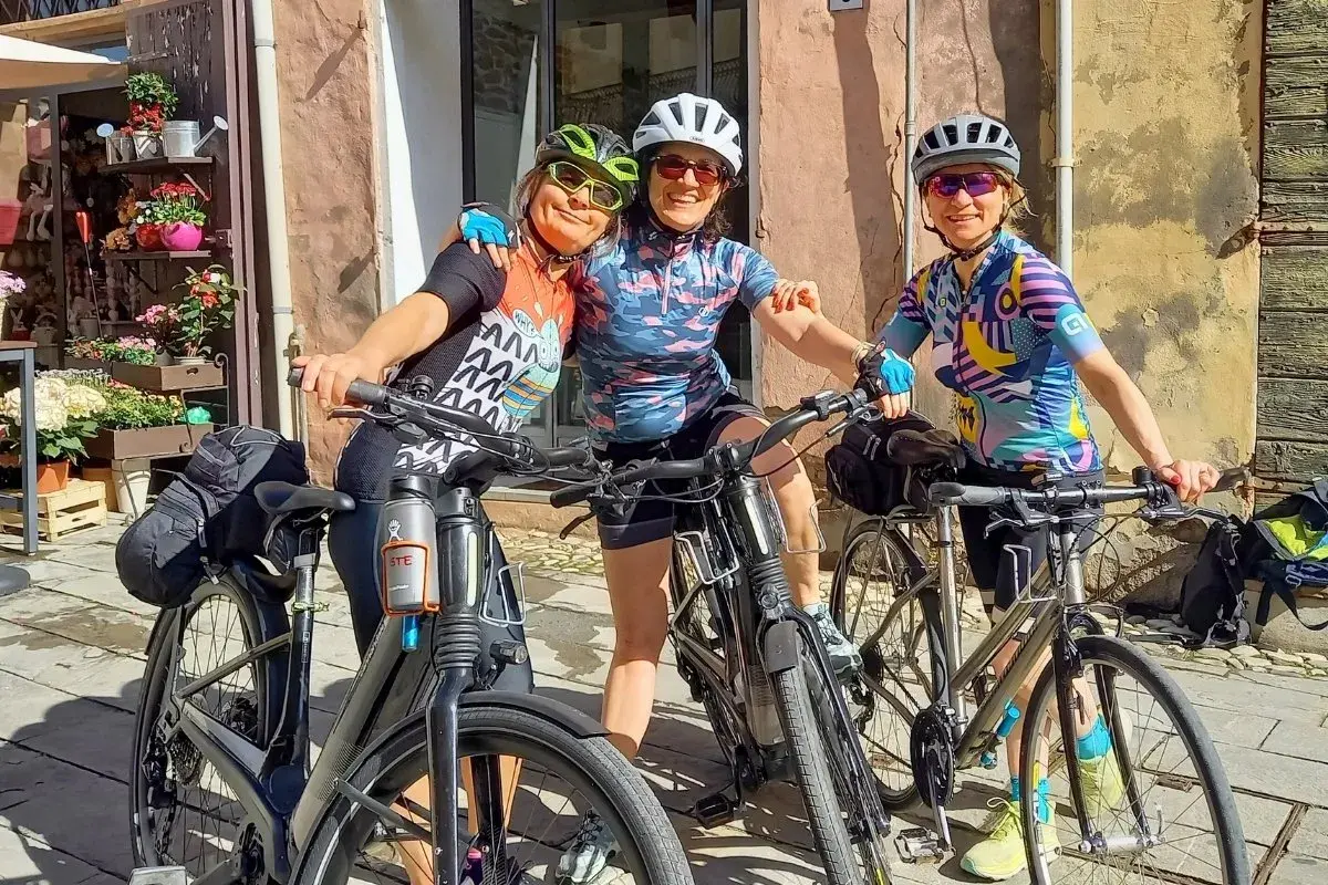 Three friends ready for guided bike tours in Europe, smiling with their bikes in front of a charming shop.