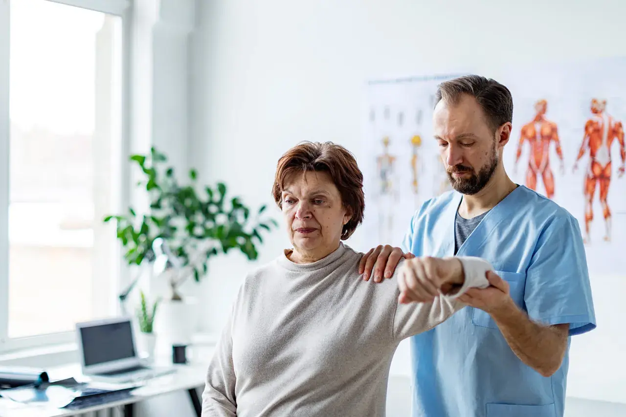 Physiotherapeut hilft einer Frau mit einer schmerzenden, verklemmten Schulter bei der Bewegung.