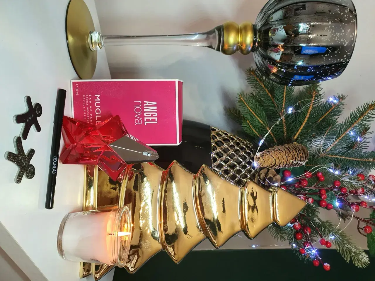 Świąteczna kompozycja z perfumami Angel Nova Mugler 50 ml, świecą, choinką i ozdobami.