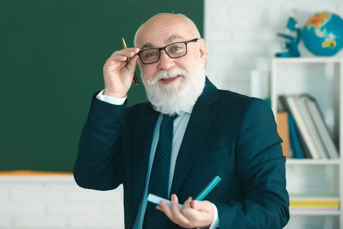 Uśmiechnięty starszy nauczyciel w okularach i garniturze trzyma długopis i marker.