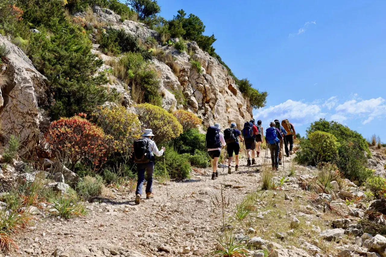 Un groupe de randonneurs explore un sentier rocailleux en Sardaigne, entouré de végétation méditerranéenne et de falaises.