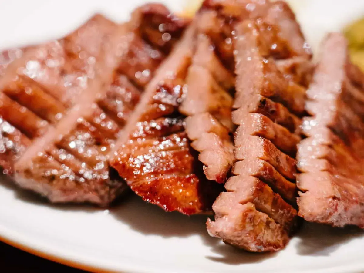 Tranches de langue de bœuf grillée, tendres et juteuses, servies sur une assiette blanche.