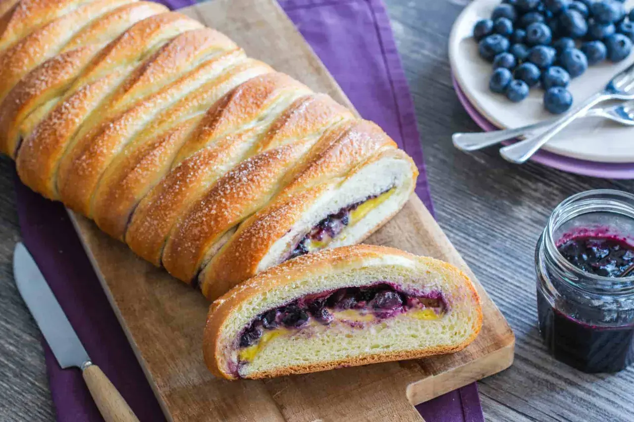 Una deliziosa treccia mochena ripiena di mirtilli e crema, cosparsa di zucchero, pronta per essere gustata.