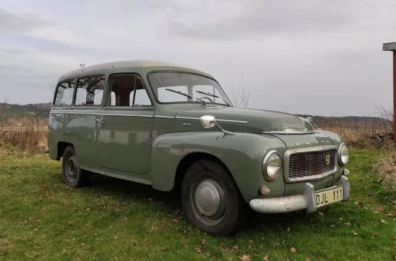Grön Volvo P210 parkerad på en gräsmatta. Bilen har en klassisk design och ser ut att vara i gott skick.