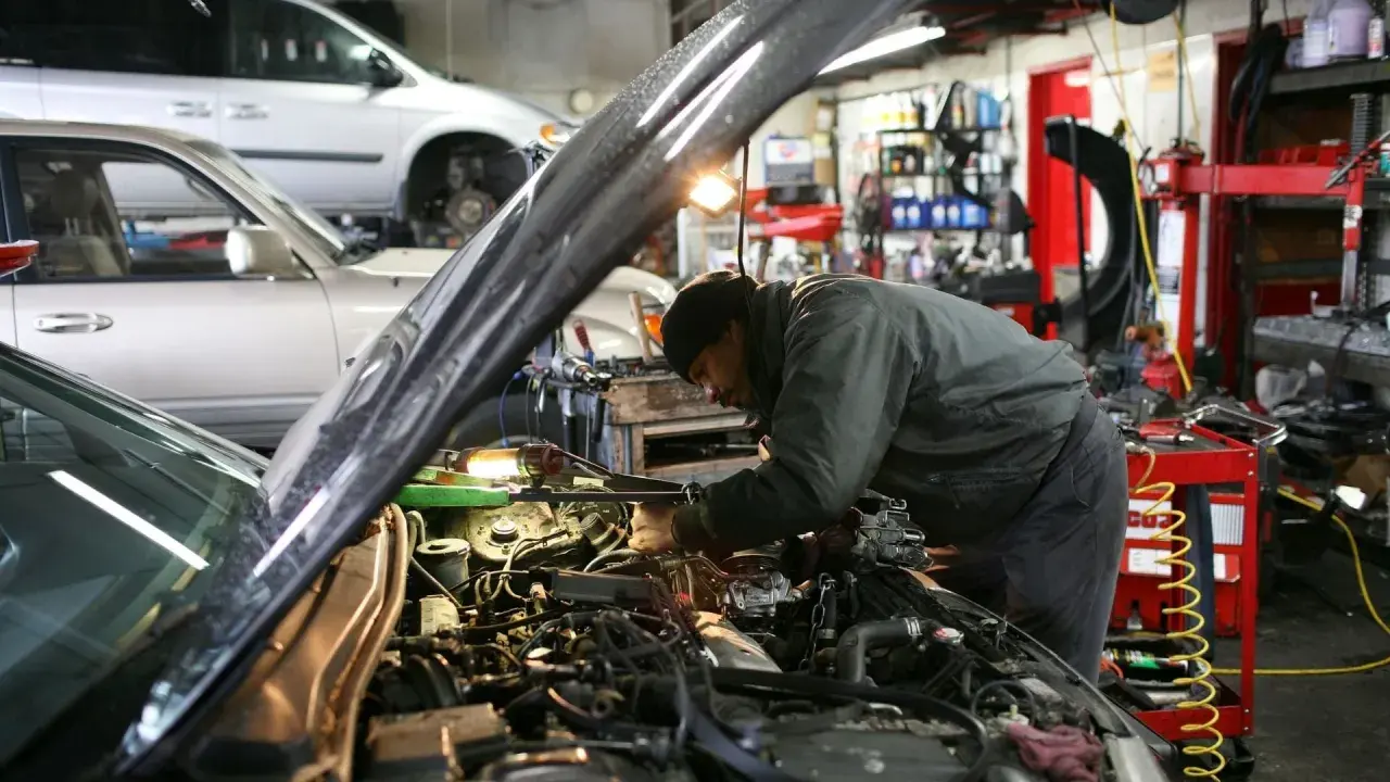 Mekaniker arbetar med en bilmotor i ett garage. En annan bil står i bakgrunden. Här erbjuds stor service.