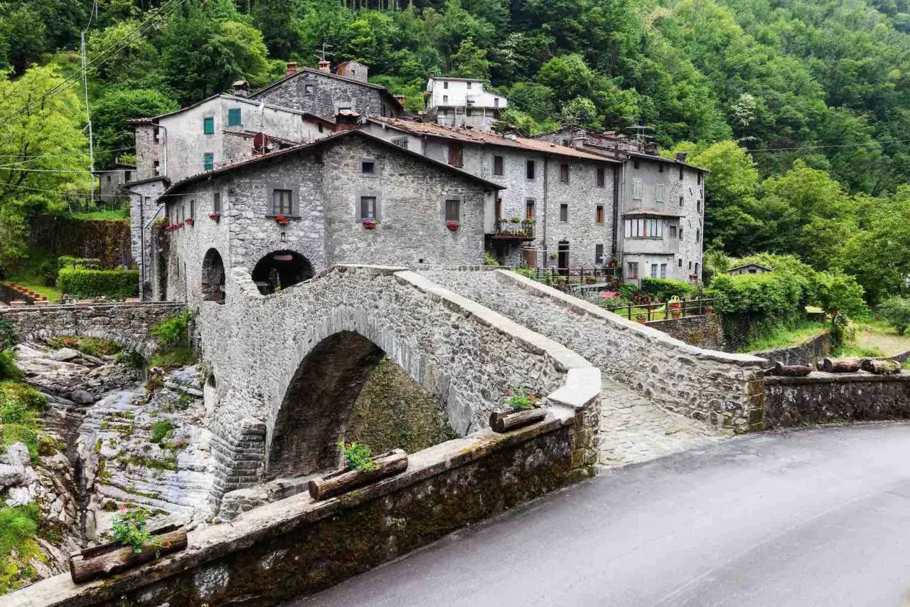 Ponte in pietra a Vergemoli, con case in pietra e vegetazione lussureggiante sullo sfondo. Le fabbriche di Vergemoli sembrano immerse nella natura.
