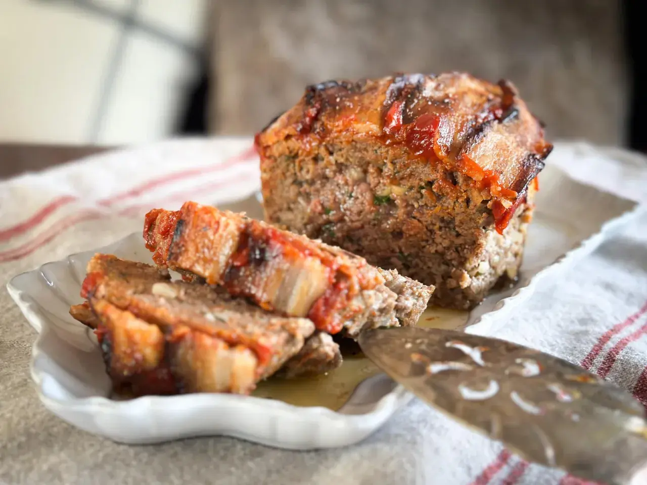 Un délicieux pain de viande, garni de tomates et de lardons, est servi sur une assiette blanche.