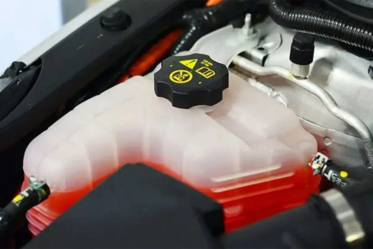Depósito de refrigerante de coche con líquido rojo. La tapa negra tiene símbolos de advertencia. Se puede echar agua normal al coche si es necesario.