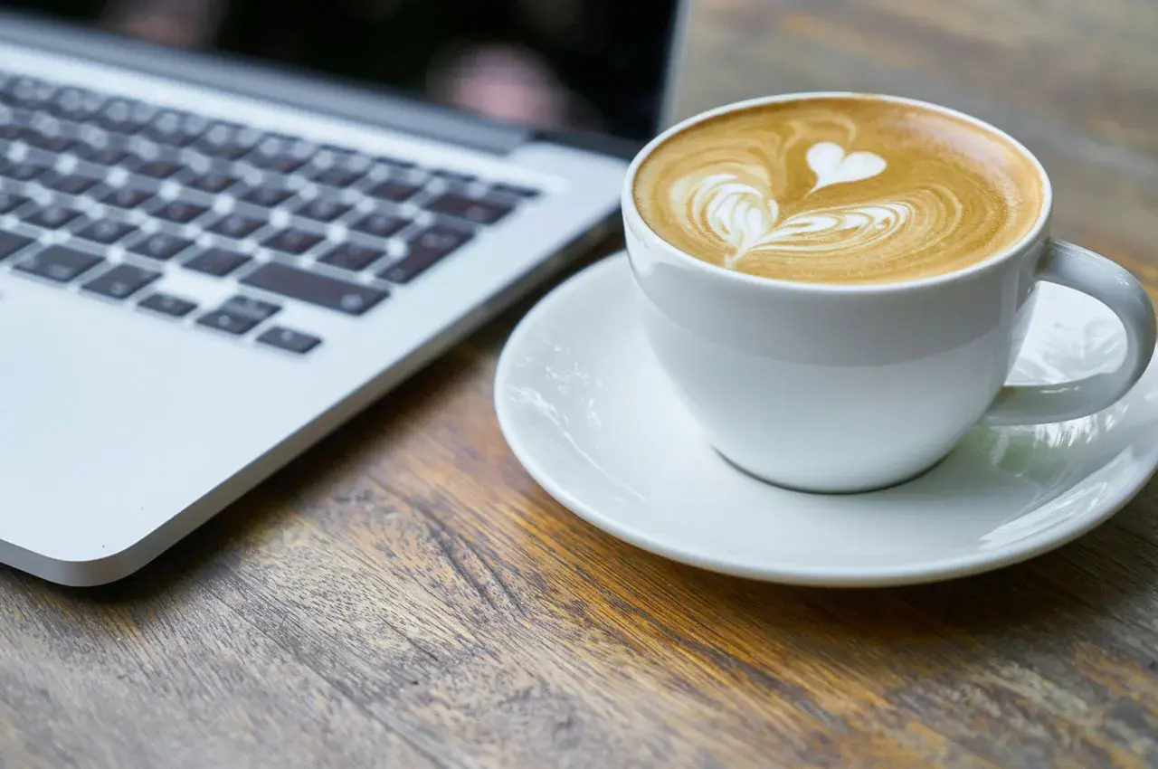 Kawa latte z sercem na piance obok laptopa. Idealny moment na picie kawy po operacji zaćmy i powrót do codzienności.