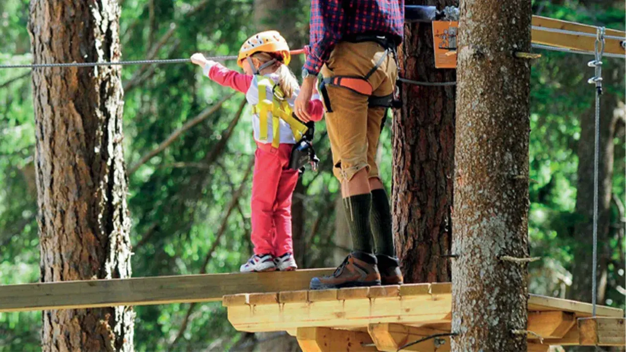 Bambina con casco giallo e adulto su passerella in un parco avventura Marche.