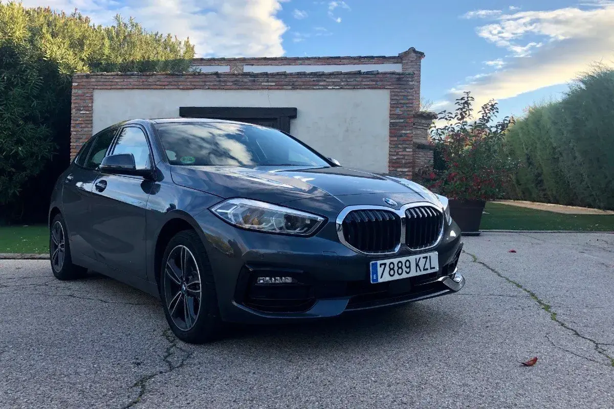 Un BMW Serie 1 116d gris aparcado frente a una casa con vegetación. A pesar de su aspecto, este modelo puede presentar problemas.
