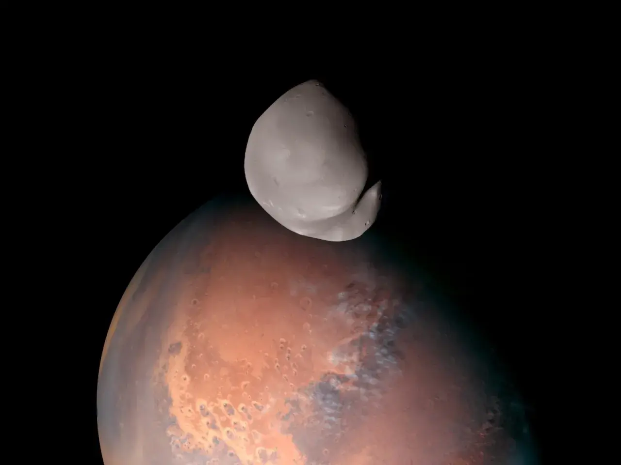 Niewielki, nieregularny księżyc Deimos unosi się nad czerwoną planetą Mars.