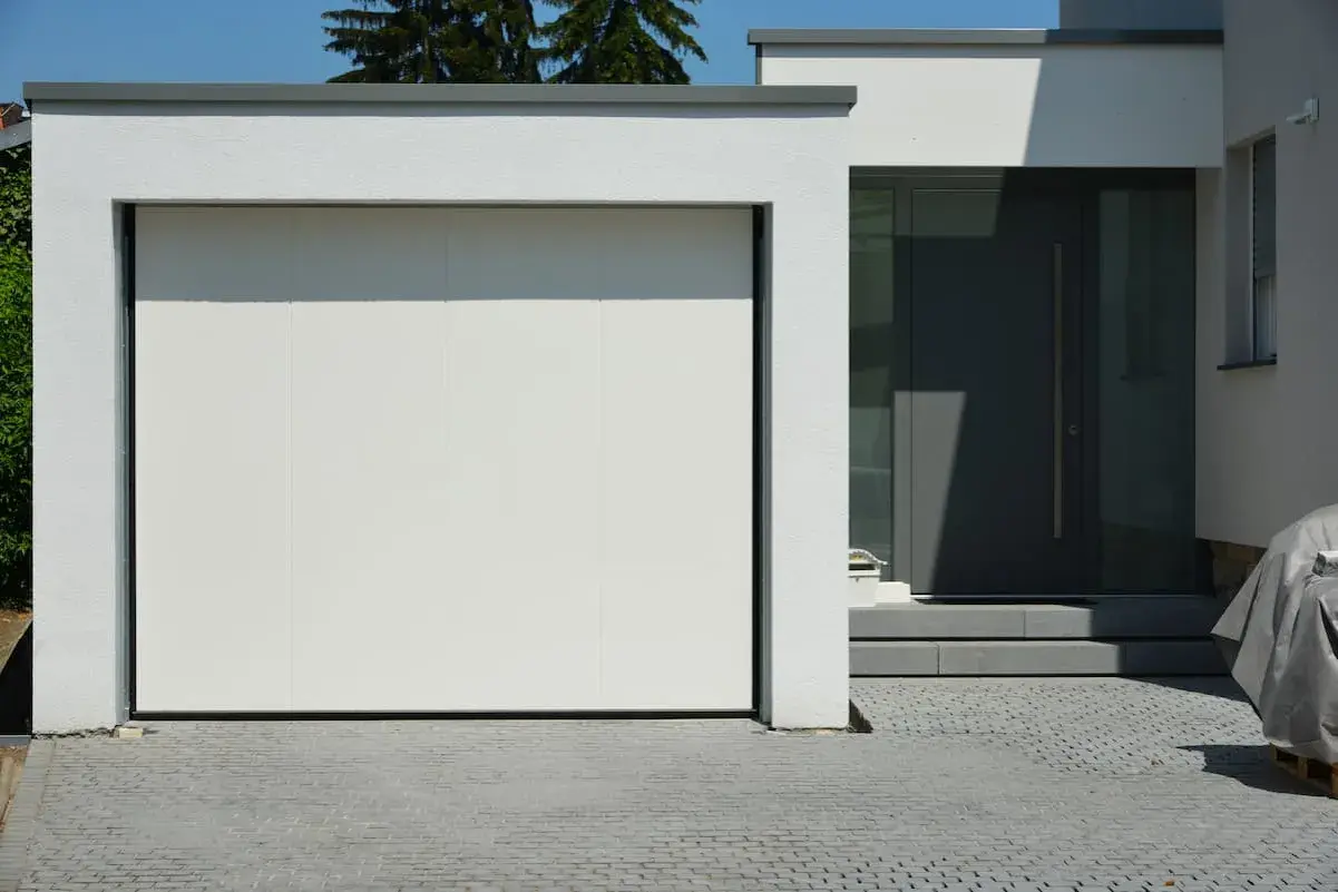 Moderne grenzbebauung mit weißer Garagentür und dunkler Eingangstür. Gepflasterte Einfahrt.